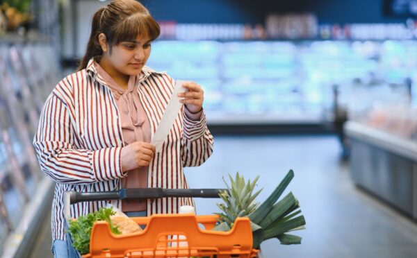 Photo shows a women reading a shopping list while pushing a trolley full of fruit and vegetables around a supermarket. A PCRM dietician says he can cut the cost of people's main holiday meal by half, provided they try a plant-based Christmas dinner