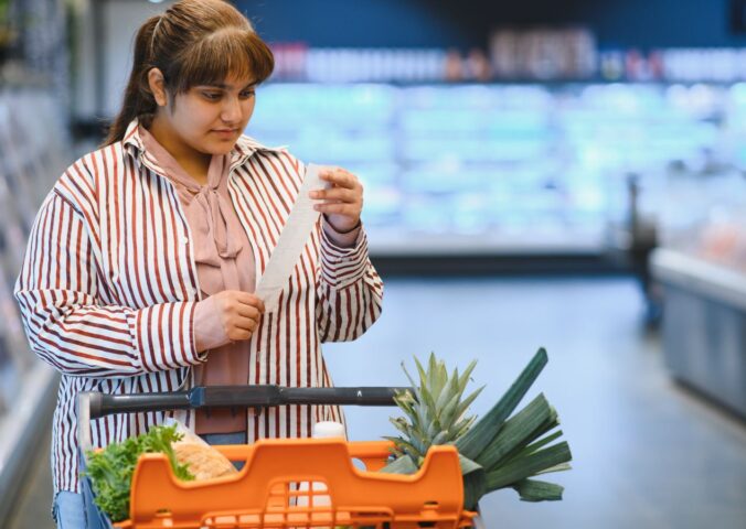 Photo shows a women reading a shopping list while pushing a trolley full of fruit and vegetables around a supermarket. A PCRM dietician says he can cut the cost of people's main holiday meal by half, provided they try a plant-based Christmas dinner