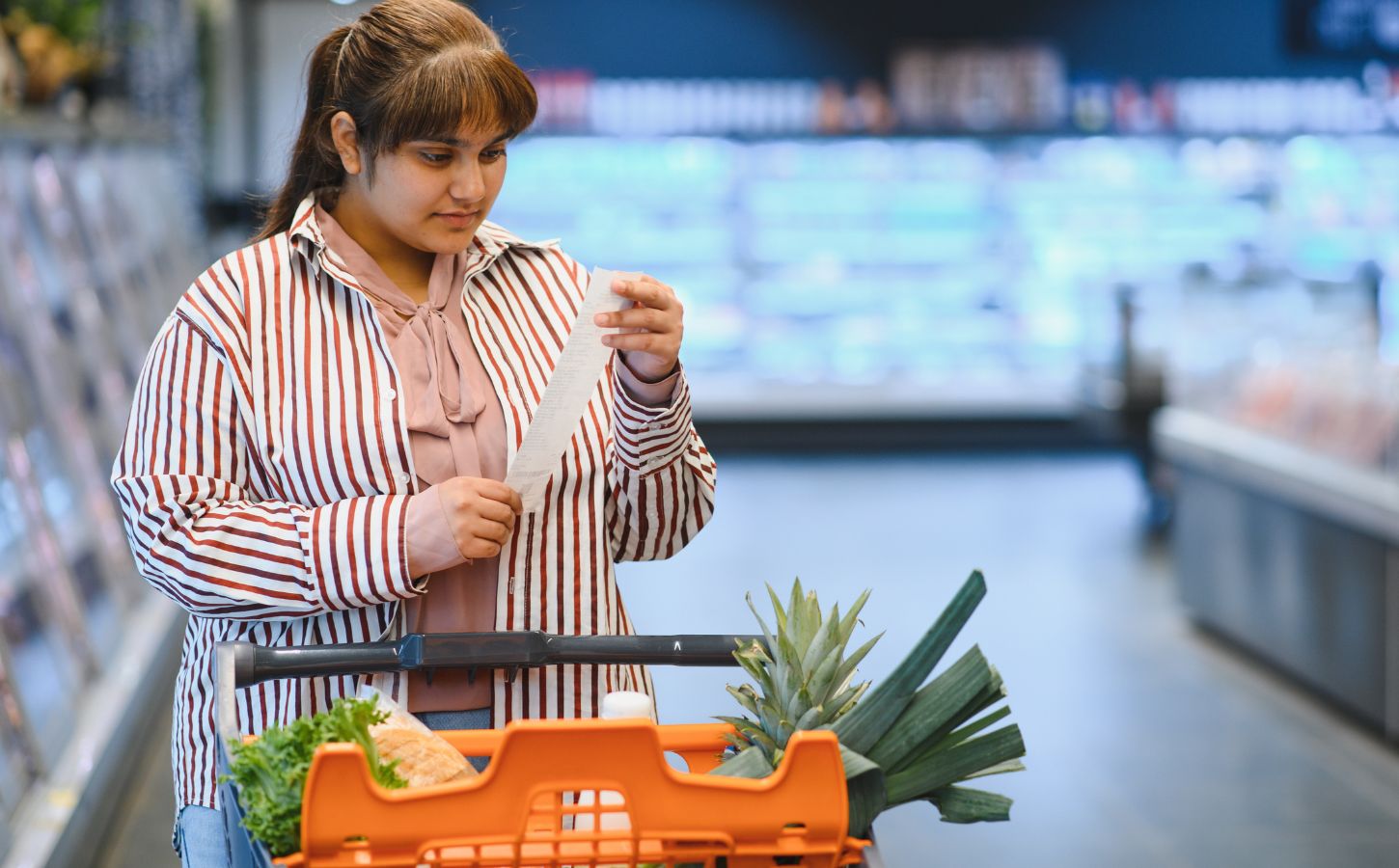 Photo shows a women reading a shopping list while pushing a trolley full of fruit and vegetables around a supermarket. A PCRM dietician says he can cut the cost of people's main holiday meal by half, provided they try a plant-based Christmas dinner