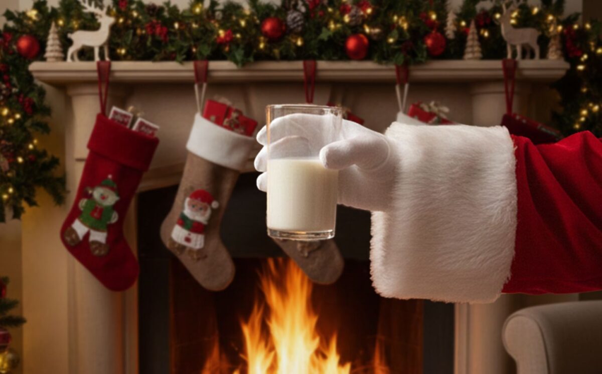 Photo shows someone dressed as Santa in a red coat with white trim and whie gloves, holding a glass of milk out in front of a fireplace and next to a decorated Christmas tree. A new survey has found tha 20 percent of people in the UK are planning to leave out plant-based milk for Santa this year