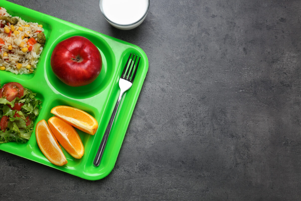 Photo shows a bright green school cafeteria tray filled with fruit, vegetables, grains, and other nutritious ingredients