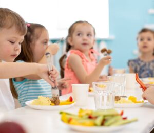 Photo shows a group of school children gathered around a healthy lunch that includes fruit and vegetables. Poland is expected to make the provision of plant-based options mandatory for all schools and nurseries