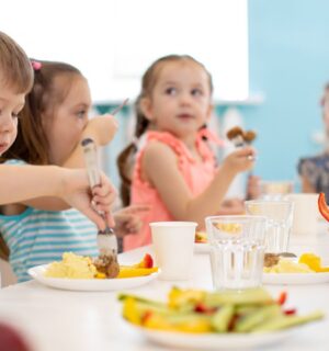 Photo shows a group of school children gathered around a healthy lunch that includes fruit and vegetables. Poland is expected to make the provision of plant-based options mandatory for all schools and nurseries