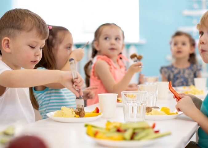 Photo shows a group of school children gathered around a healthy lunch that includes fruit and vegetables. Poland is expected to make the provision of plant-based options mandatory for all schools and nurseries
