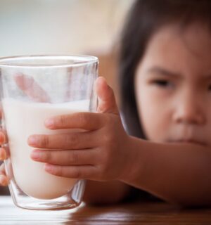 Photo shows a little girl reaching for a large glass of milk with both hands. The UK's sugar tax will now apply to sweetened plant-based milks, effectively giving traditional dairy an advantage