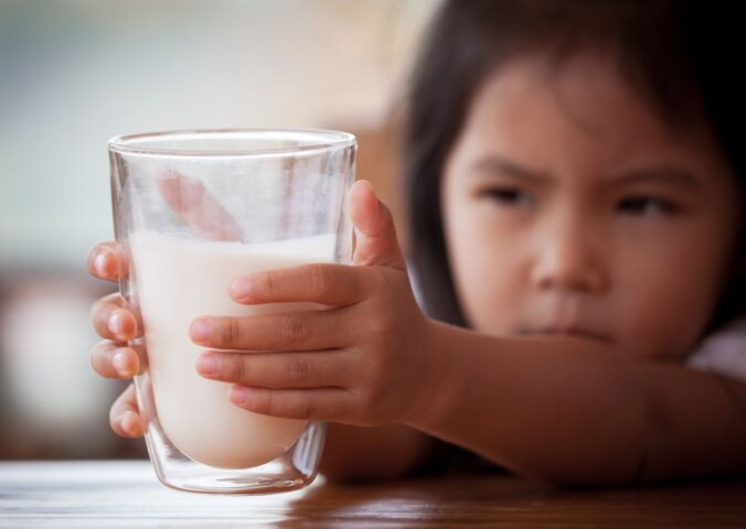 Photo shows a little girl reaching for a large glass of milk with both hands. The UK's sugar tax will now apply to sweetened plant-based milks, effectively giving traditional dairy an advantage
