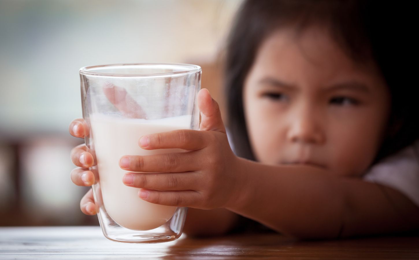 Photo shows a little girl reaching for a large glass of milk with both hands. The UK's sugar tax will now apply to sweetened plant-based milks, effectively giving traditional dairy an advantage