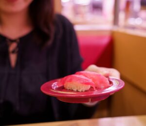 Photo shows a young Japanese woman holding up a plate of sushi made with tuna fish. According to a new report, urban flexitarians are behind the vegan tuna boom in Japan
