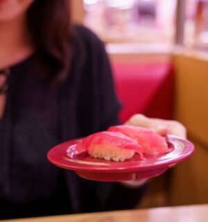 Photo shows a young Japanese woman holding up a plate of sushi made with tuna fish. According to a new report, urban flexitarians are behind the vegan tuna boom in Japan