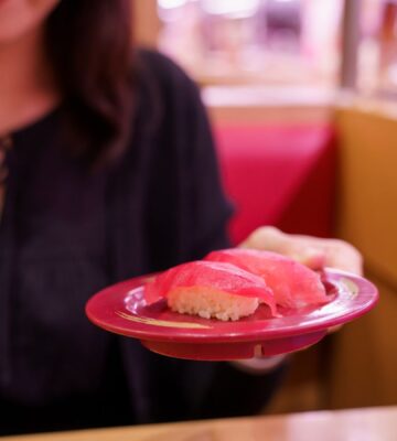 Photo shows a young Japanese woman holding up a plate of sushi made with tuna fish. According to a new report, urban flexitarians are behind the vegan tuna boom in Japan