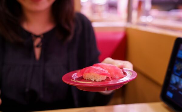 Photo shows a young Japanese woman holding up a plate of sushi made with tuna fish. According to a new report, urban flexitarians are behind the vegan tuna boom in Japan