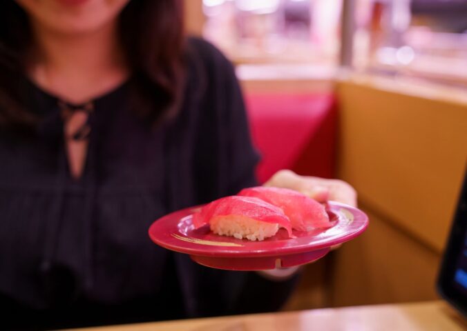 Photo shows a young Japanese woman holding up a plate of sushi made with tuna fish. According to a new report, urban flexitarians are behind the vegan tuna boom in Japan