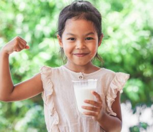 Photo shows a child flexing her bicep and holding a glass of milk. The US Senate just passed a bill that gives children access to plant-based milk in school