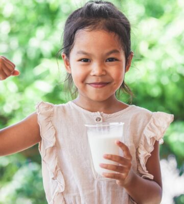 Photo shows a child flexing her bicep and holding a glass of milk. The US Senate just passed a bill that gives children access to plant-based milk in school