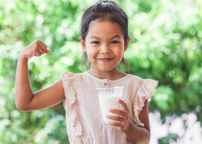 Photo shows a child flexing her bicep and holding a glass of milk. The US Senate just passed a bill that gives children access to plant-based milk in school