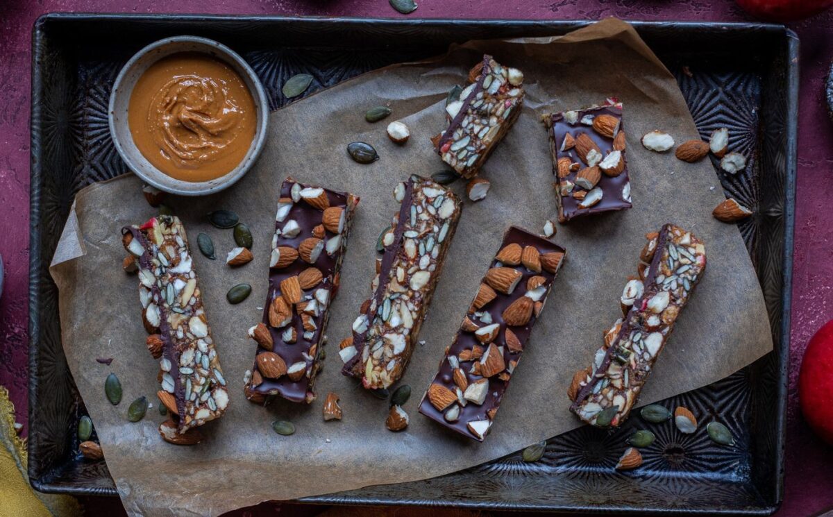 Vegan energy bars on a baking tray next to some apples and nut butter for snacky sweets
