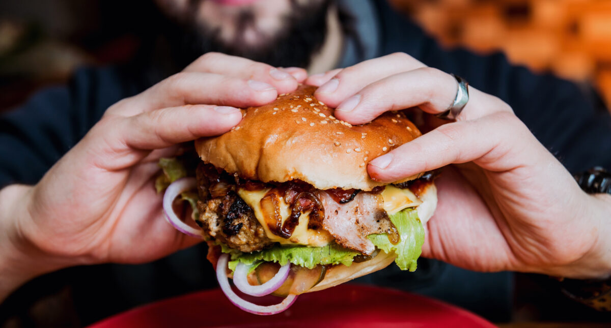 Photo shows someone's hands as he eats a large cheeseburger made with animal products