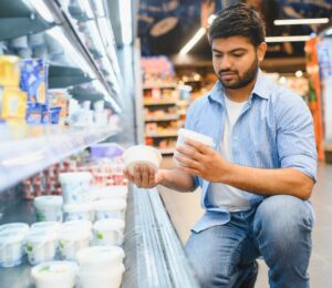Photo shows a young man reading different yoghurt containers in the supermarket. Different diets have different impacts on the planet, and generally, the more animal products you eat, the bigger your impact on the planet
