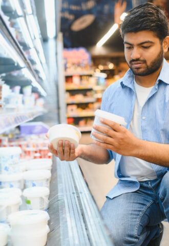 Photo shows a young man reading different yoghurt containers in the supermarket. Different diets have different impacts on the planet, and generally, the more animal products you eat, the bigger your impact on the planet