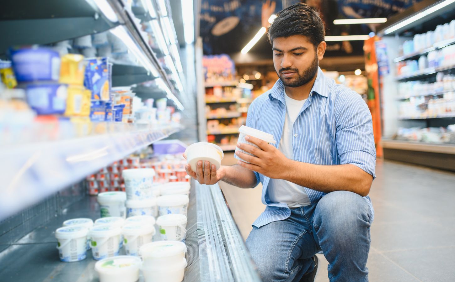 Photo shows a young man reading different yoghurt containers in the supermarket. Different diets have different impacts on the planet, and generally, the more animal products you eat, the bigger your impact on the planet