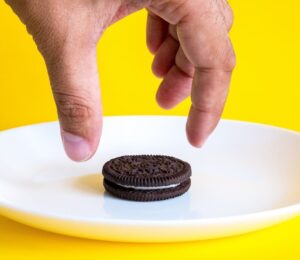 Photo shows someone's hand reaching for an Oreo on a white plate against a bright yellow background. Mondelēz International, the major confectionary multinational behind Oreos, has officially ceased all animal testing