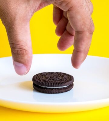 Photo shows someone's hand reaching for an Oreo on a white plate against a bright yellow background. Mondelēz International, the major confectionary multinational behind Oreos, has officially ceased all animal testing