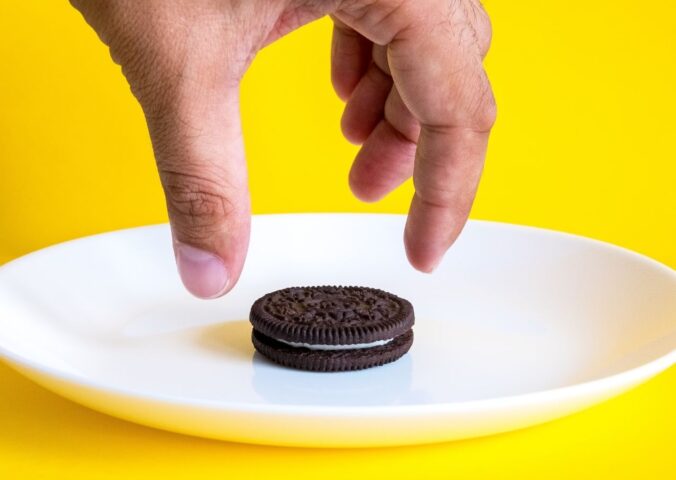 Photo shows someone's hand reaching for an Oreo on a white plate against a bright yellow background. Mondelēz International, the major confectionary multinational behind Oreos, has officially ceased all animal testing