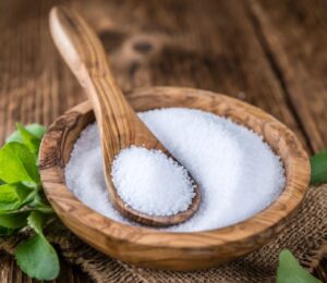 Stevia in plant and granular form on a spoon in a wooden bowl to illustrate the question explored in the article: is stevia safe?