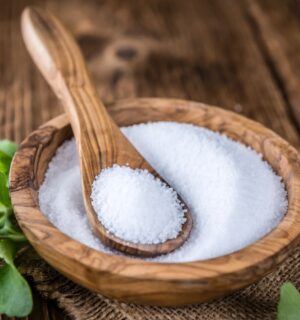 Stevia in plant and granular form on a spoon in a wooden bowl to illustrate the question explored in the article: is stevia safe?