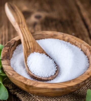 Stevia in plant and granular form on a spoon in a wooden bowl to illustrate the question explored in the article: is stevia safe?