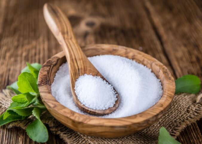 Stevia in plant and granular form on a spoon in a wooden bowl to illustrate the question explored in the article: is stevia safe?