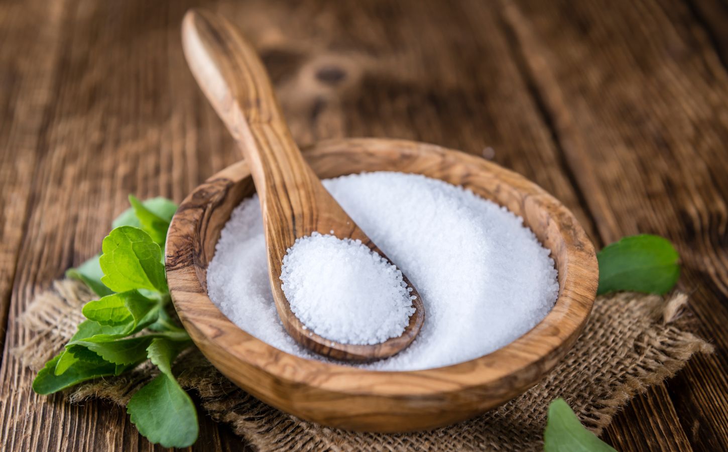 Stevia in plant and granular form on a spoon in a wooden bowl to illustrate the question explored in the article: is stevia safe?