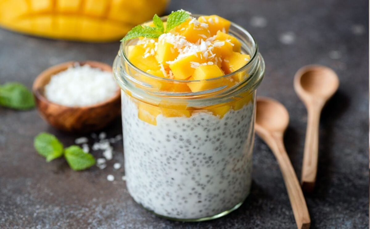 Healthy chia coconut pudding with mango in glass jar and two wooden spoons on a dark background to illustrate the fibermaxxing trend