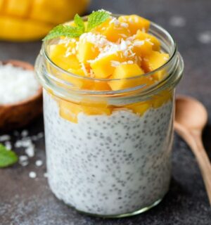 Healthy chia coconut pudding with mango in glass jar and two wooden spoons on a dark background to illustrate the fibermaxxing trend
