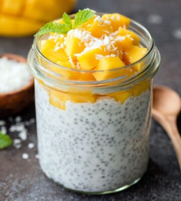 Healthy chia coconut pudding with mango in glass jar and two wooden spoons on a dark background to illustrate the fibermaxxing trend