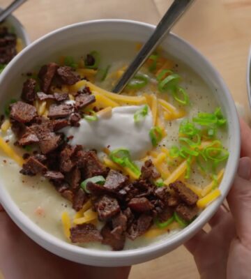 A bowl of loaded baked potato soup topped with smoky tofu bacon, vegan cheese, and scallions, one of Sarah Sullivan’s cozy vegan winter soups
