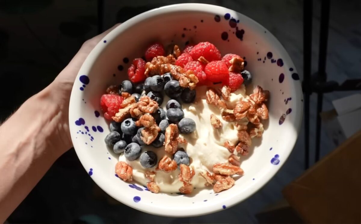 A close-up of Merle's hand holding the vegan yogurt bowl topped with fruit and nuts, a perfect vegan comfort meals
