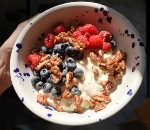 A close-up of Merle's hand holding the vegan yogurt bowl topped with fruit and nuts, a perfect vegan comfort meals