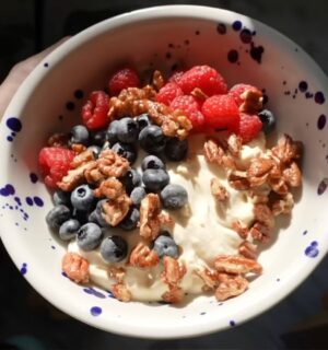 A close-up of Merle's hand holding the vegan yogurt bowl topped with fruit and nuts, a perfect vegan comfort meals
