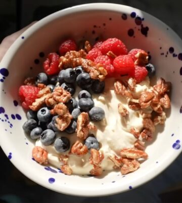A close-up of Merle's hand holding the vegan yogurt bowl topped with fruit and nuts, a perfect vegan comfort meals