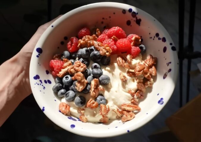 A close-up of Merle's hand holding the vegan yogurt bowl topped with fruit and nuts, a perfect vegan comfort meals