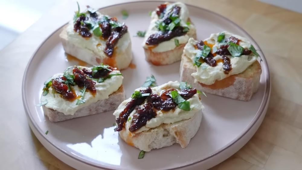 Slices of toasted bread topped with vegan ricotta and garnishes on a plate, presented as one of 3 vegan comfort foods