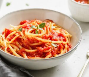 A bowl of spaghetti with tomato sauce and fresh basil on a white table, part of what Dr Neal Barnard eats in a day