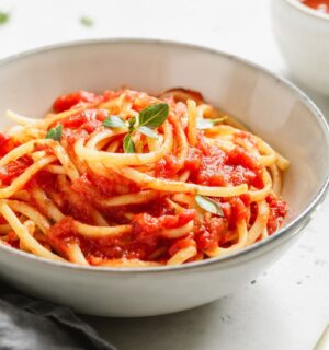 A bowl of spaghetti with tomato sauce and fresh basil on a white table, part of what Dr Neal Barnard eats in a day