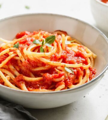 A bowl of spaghetti with tomato sauce and fresh basil on a white table, part of what Dr Neal Barnard eats in a day