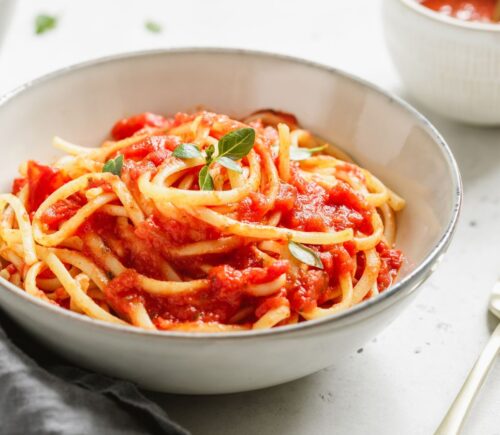 A bowl of spaghetti with tomato sauce and fresh basil on a white table, part of what Dr Neal Barnard eats in a day
