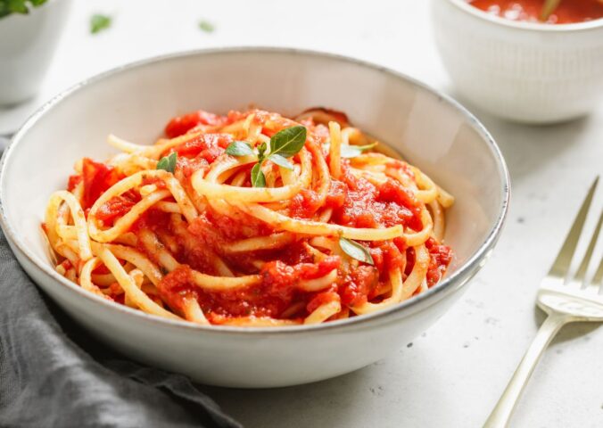 A bowl of spaghetti with tomato sauce and fresh basil on a white table, part of what Dr Neal Barnard eats in a day
