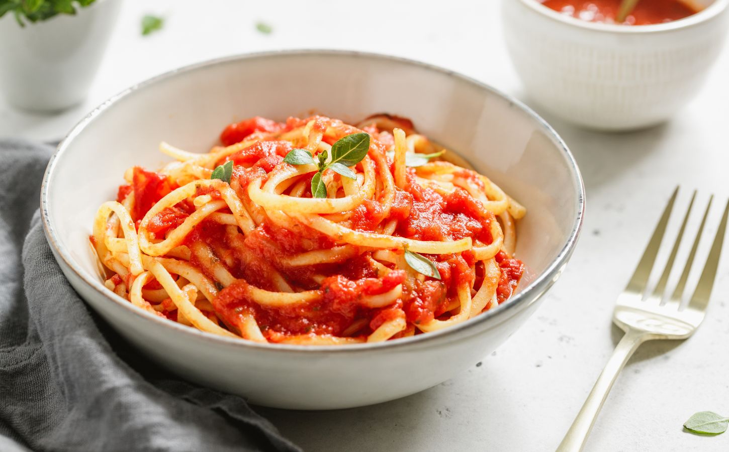 A bowl of spaghetti with tomato sauce and fresh basil on a white table, part of what Dr Neal Barnard eats in a day