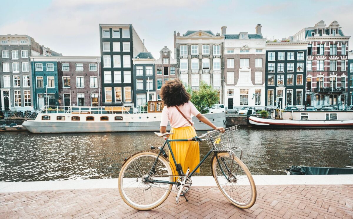 Photo shows a young woman on a bicycle by a canal in Amsterdam, Netherlands. Amsterdam just became the first capital city in the world to ban ads for meat and fossil fuel related products in public spaces