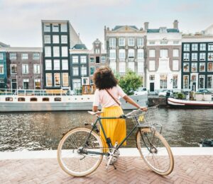 Photo shows a young woman on a bicycle by a canal in Amsterdam, Netherlands. Amsterdam just became the first capital city in the world to ban ads for meat and fossil fuel related products in public spaces